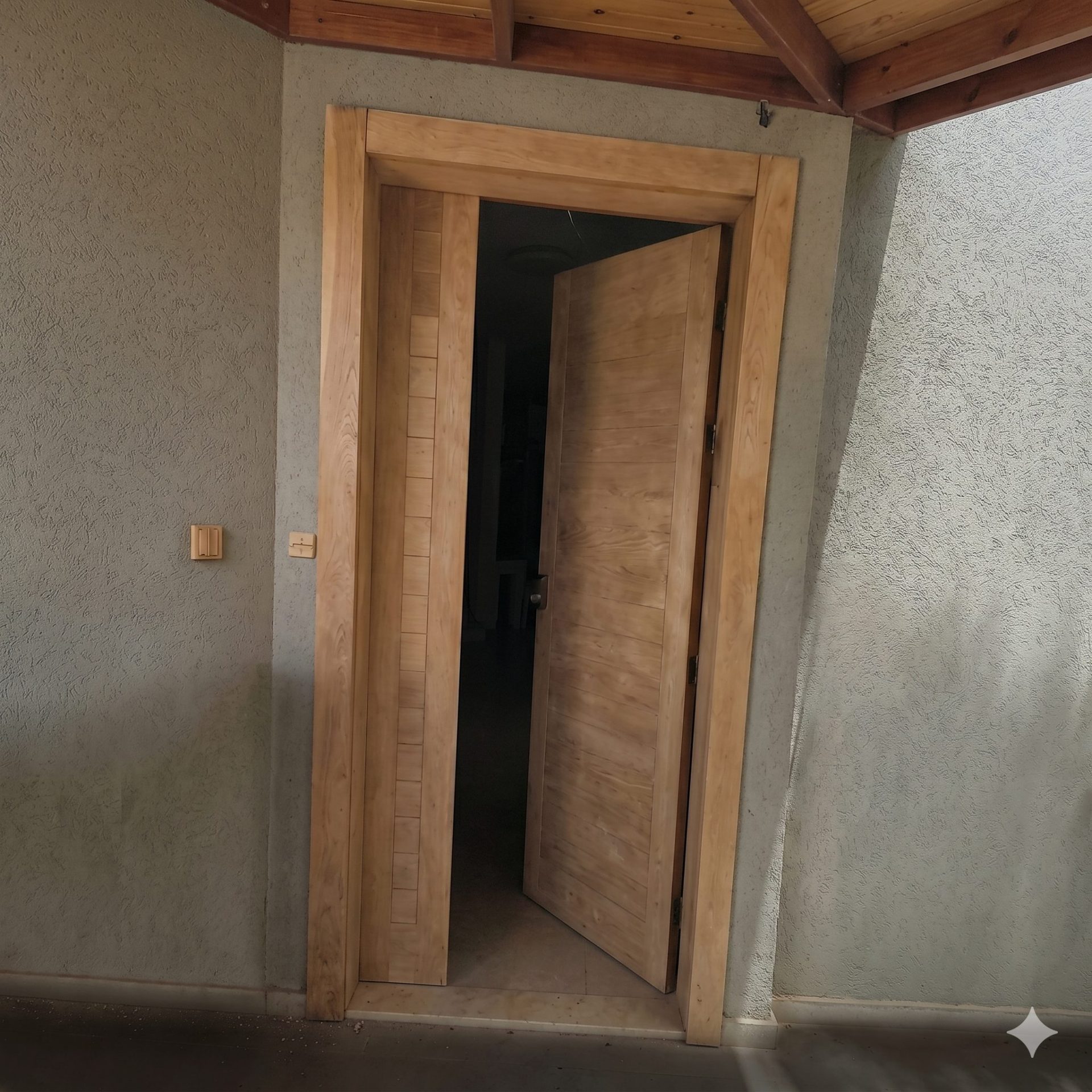 דלת העץ במצב פתוח למחצה, החושף את פנים הבית החשוך ומציג את גוון העץ הטבעי והבהיר של הלוחות והמשקוף.