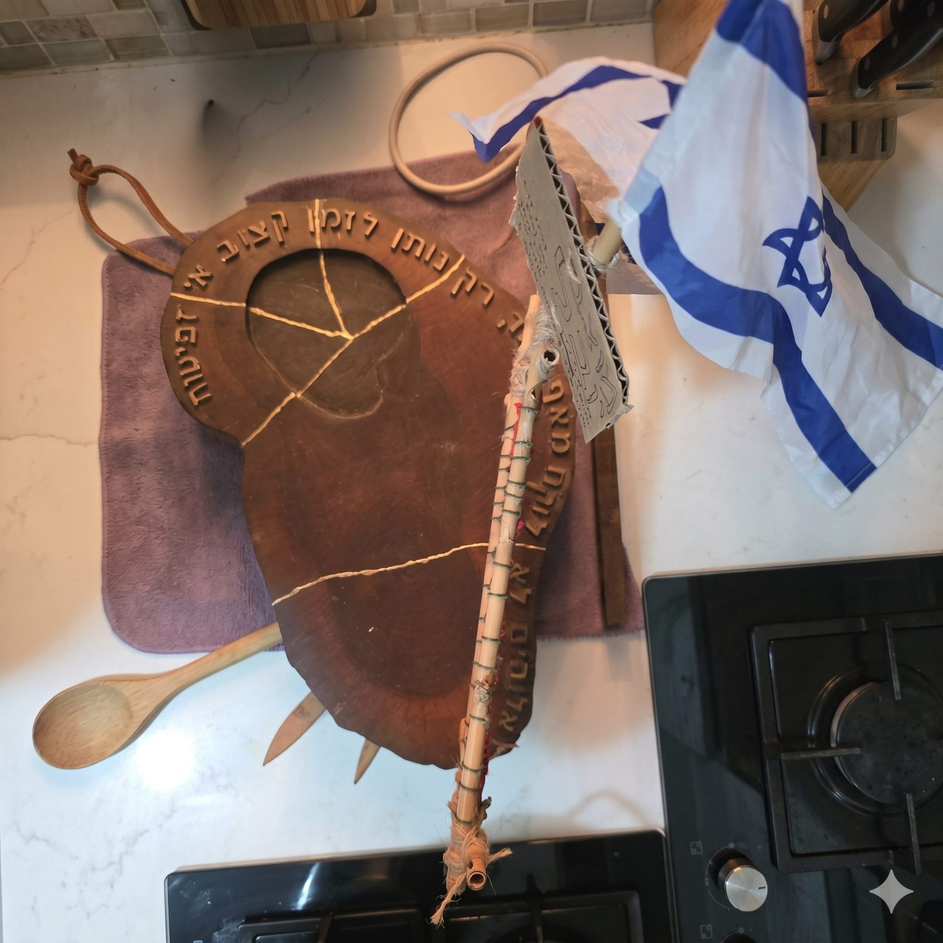 מיצג פיסולי מעץ עם דמויות מנגנות והשורה החרוטה "מאה אלו השירים", מצולם על שולחן העבודה בסטודיו לצד מכחולים וצבעים.